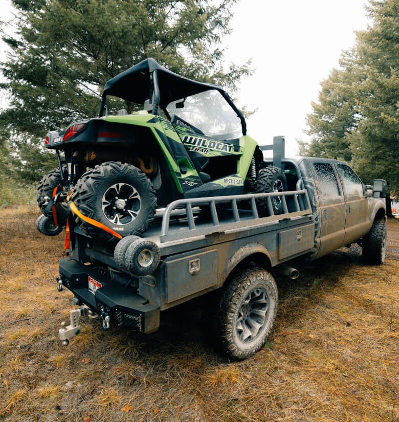 A black TUFFLIFT flatbed holding a green side-by-side among pine trees in North Idaho